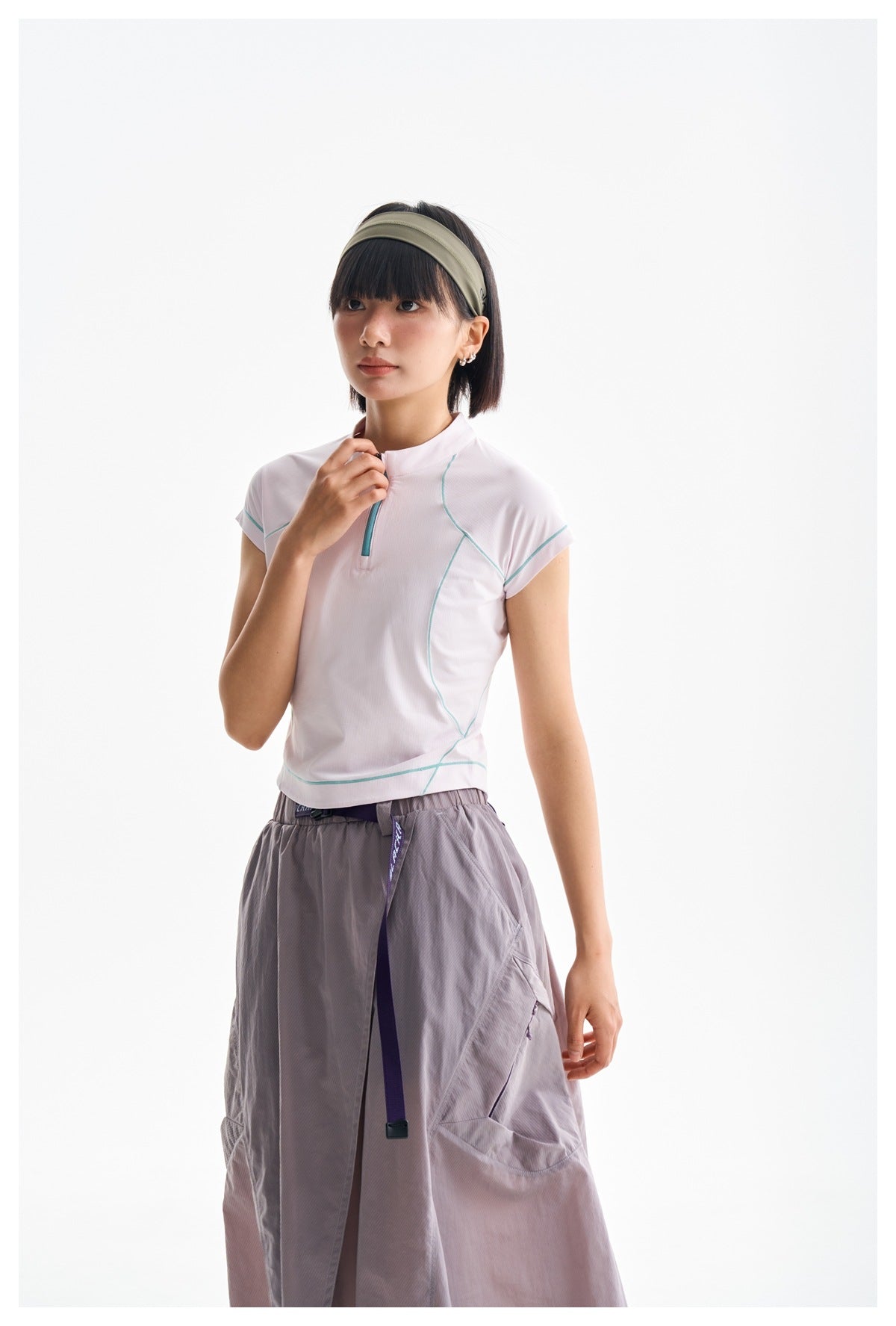 Model wearing a pale pink zip-neck top with teal piping and a gray-lilac skirt.