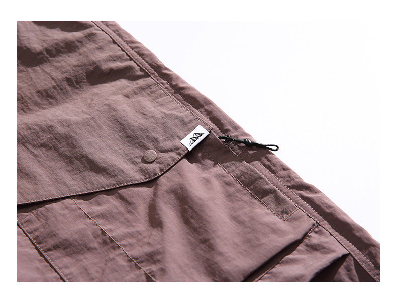 Close-up of brown shorts showing a flap pocket, button, stitched seams and a small sewn-in tag.