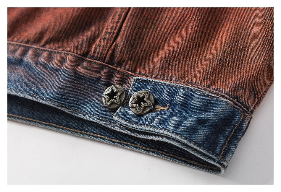 Close-up of a rust-red denim jacket hem with a blue-washed band and two ornate star buttons.