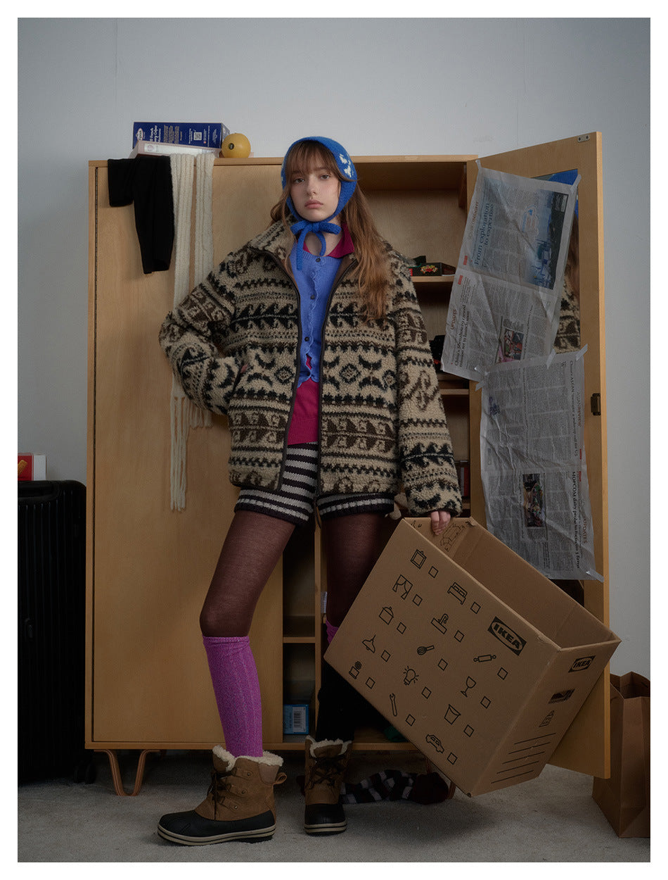 Model wearing patterned fleece-texture zip jacket over a blue cardigan with a blue hat, standing by a wooden wardrobe