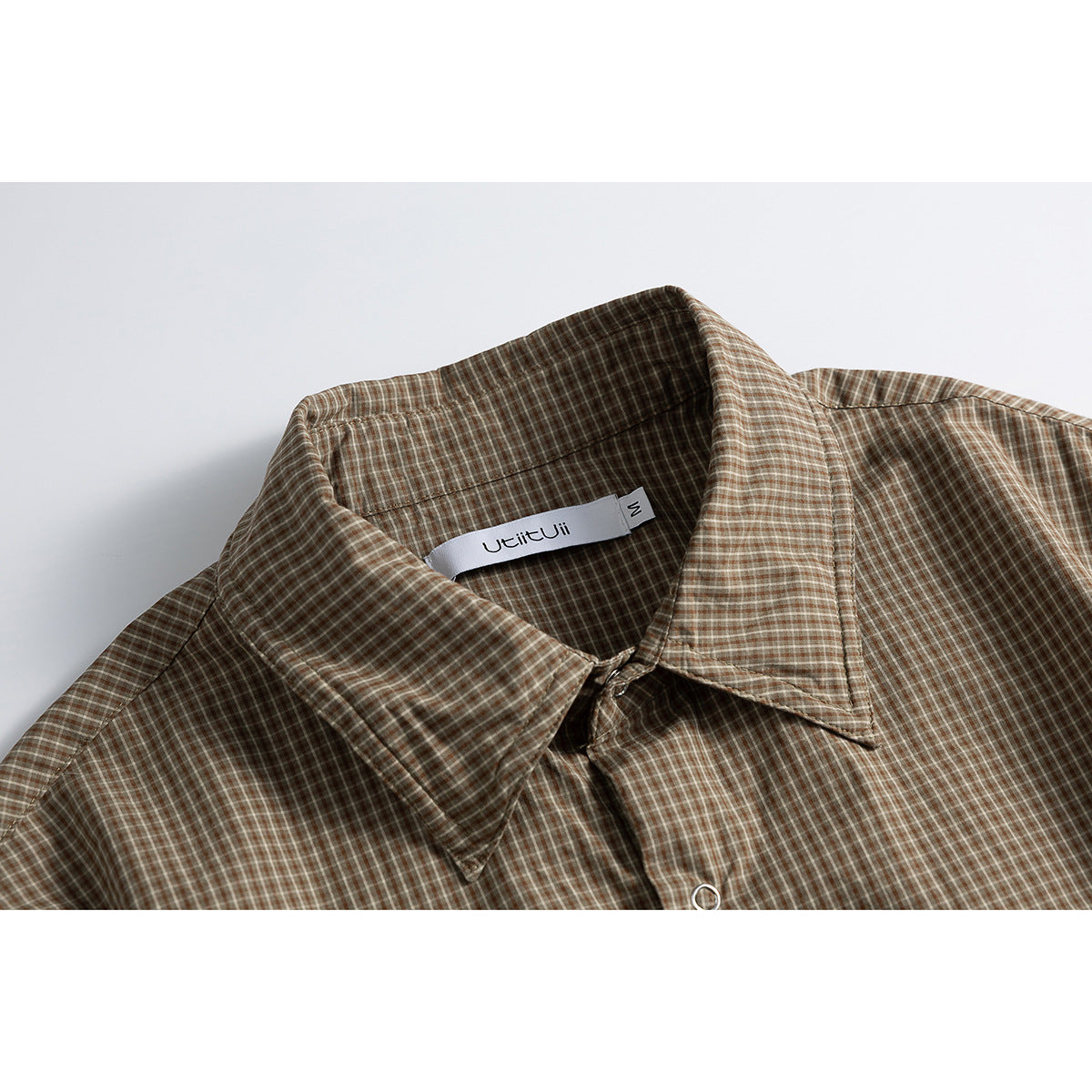Close-up of a brown and beige checked shirt collar, with a sewn-in neck label and a metal button.