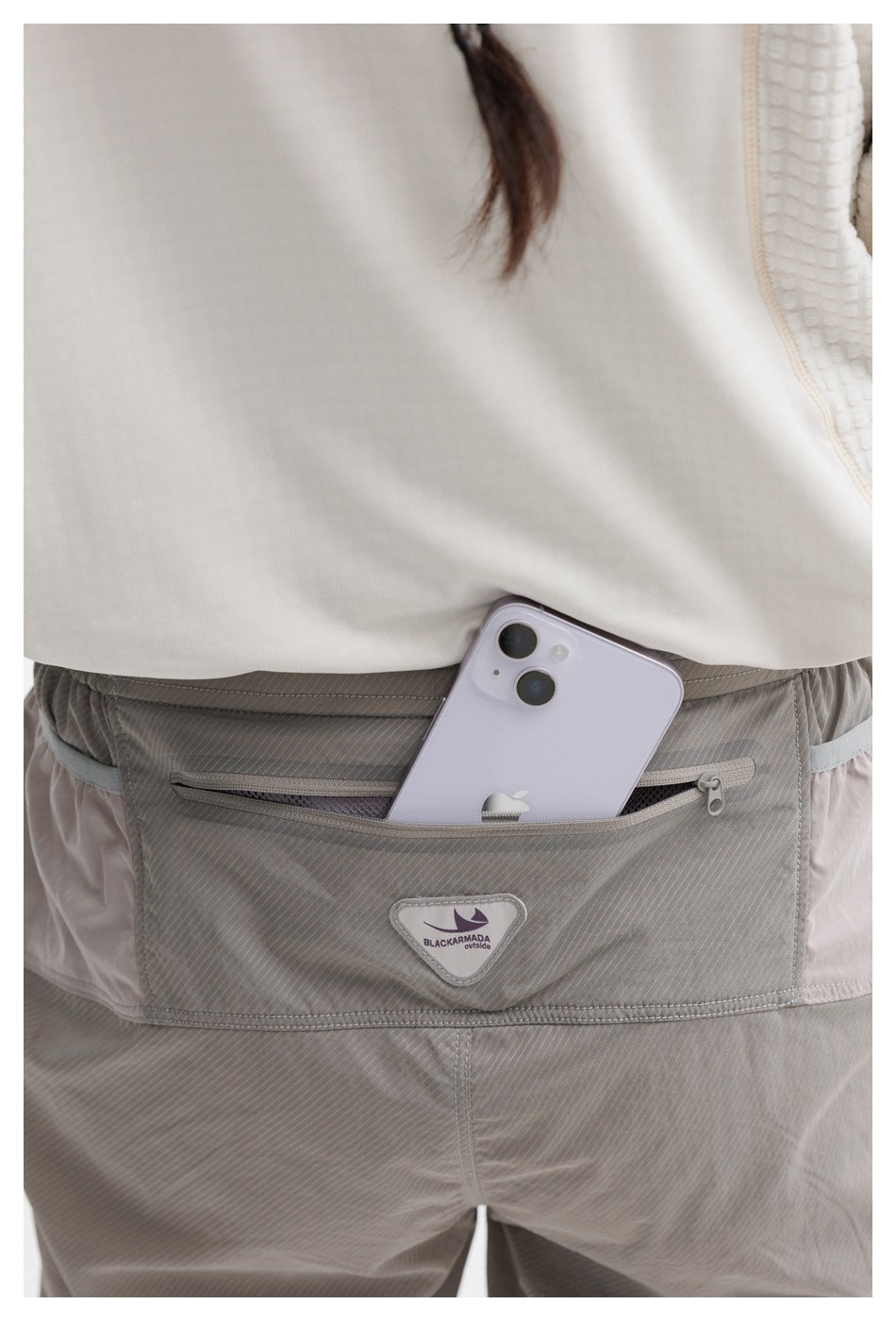 Close-up of the gray pants' rear zip pocket, with a phone tucked inside and a small sewn label below.
