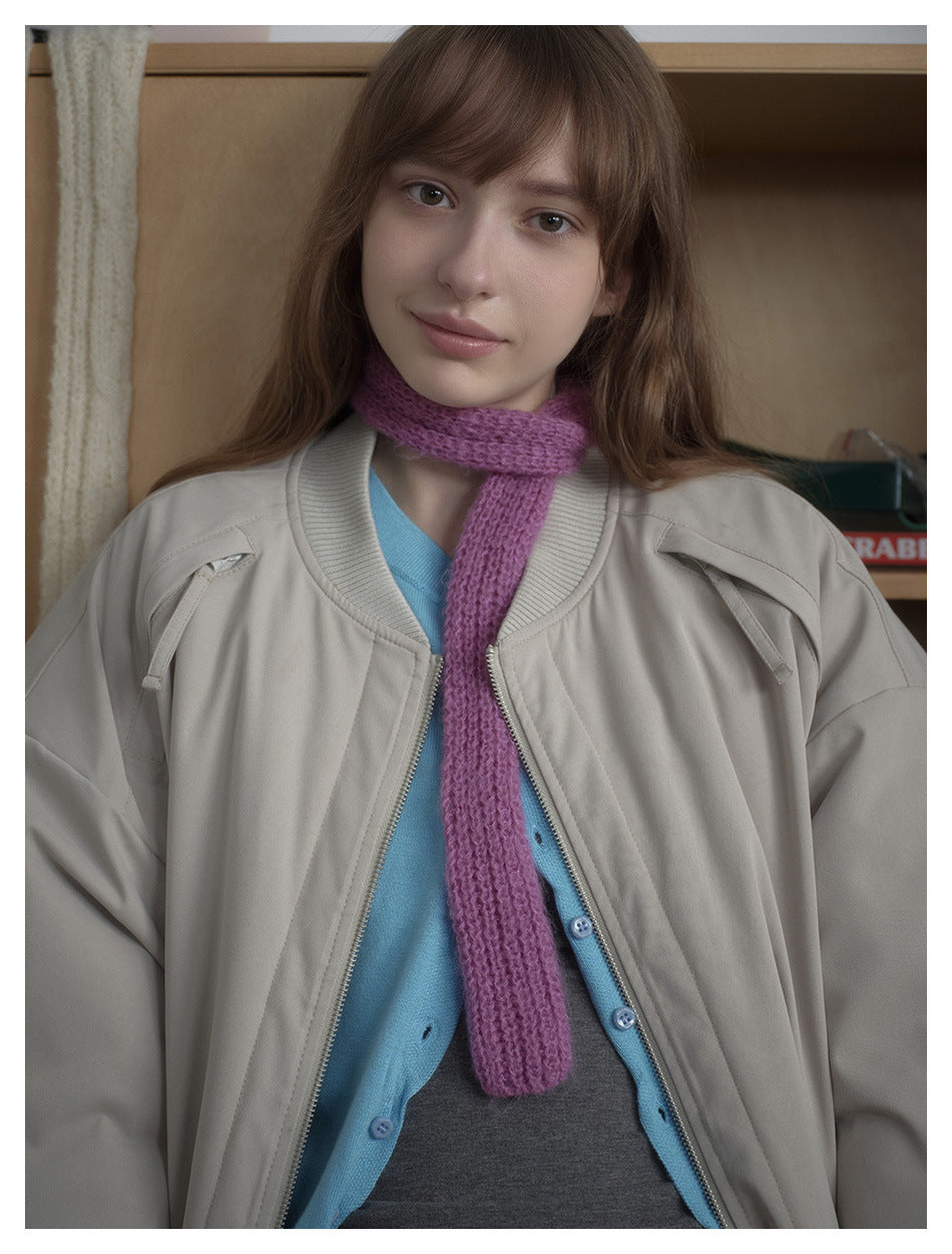 Close view of a model wearing a light beige-gray jacket with a ribbed collar over a blue cardigan and purple scarf.