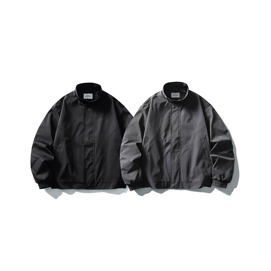 Front views of two stand-collar jackets, one black and one charcoal, with snap closures and angled pockets.