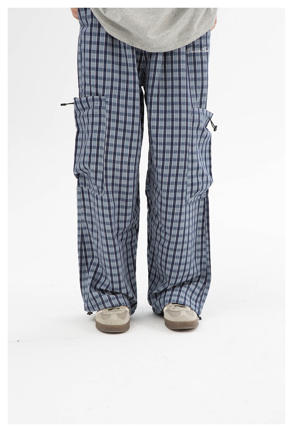 Close-up of blue plaid wide-leg pants worn with sneakers, showing thigh pockets with toggle drawcords and hem cords