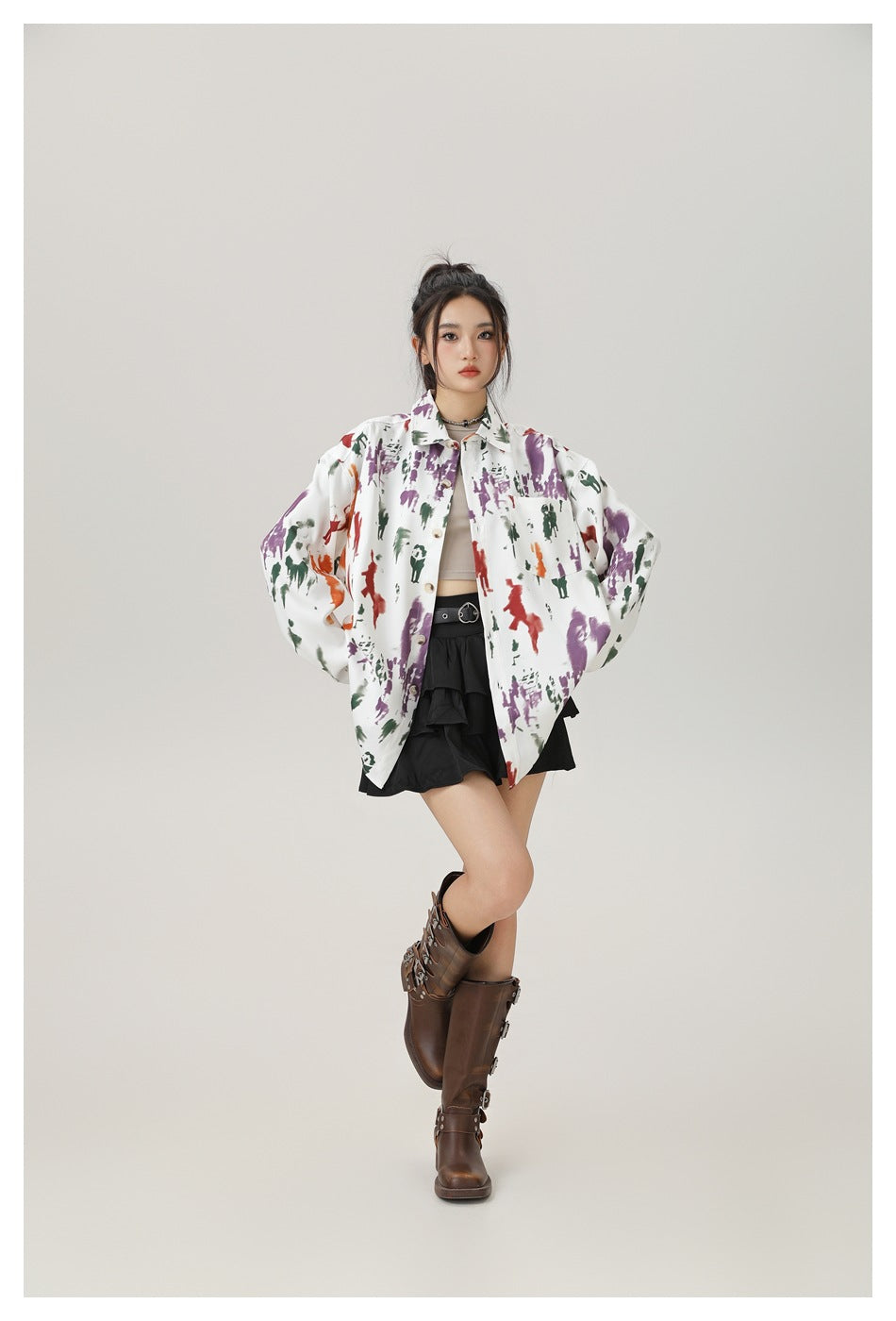 Full-length view of a model in an oversized printed shirt worn open with a black skirt and brown boots