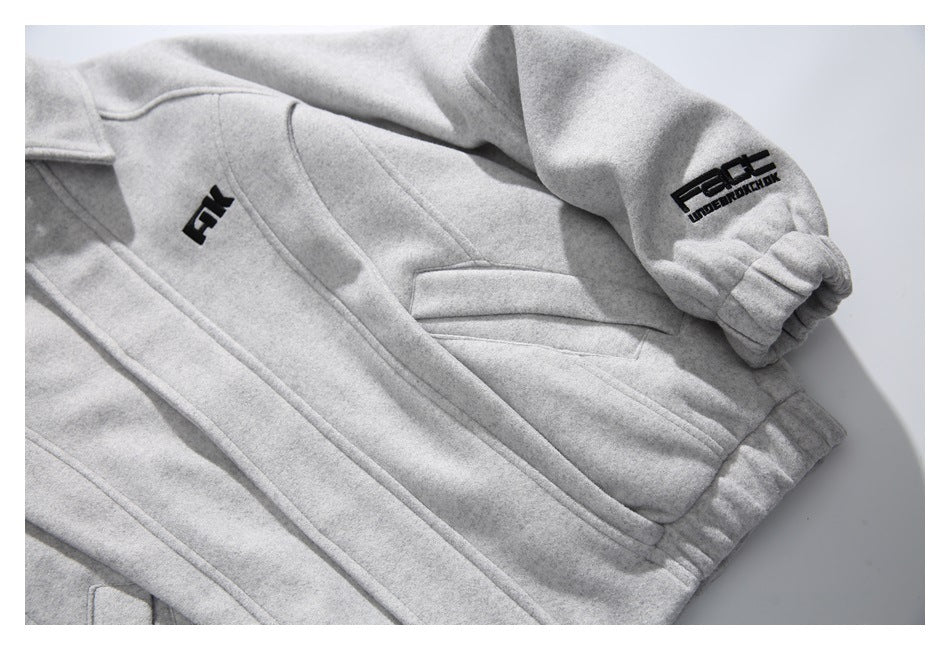 Close-up of the light gray jacket's front seams, angled pocket, elastic cuff, and black sleeve graphic.
