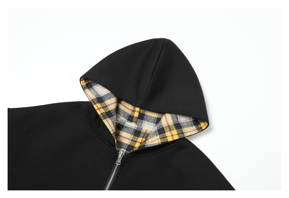 Close-up of a black zip-up hoodie with a yellow, gray, and cream plaid lining inside the hood.