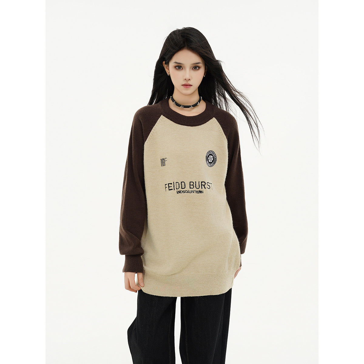 Front view of a model in a cream raglan sweater with dark brown sleeves, ribbed trim and chest graphics.