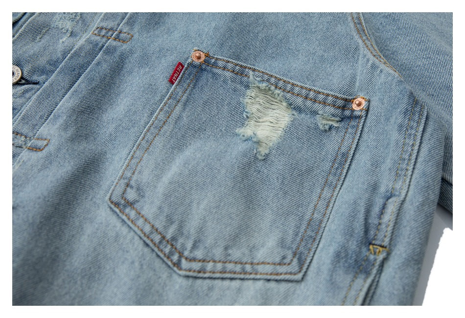 Close-up of a light-wash denim jacket pocket with frayed distressing, copper rivets, and a small red tab.