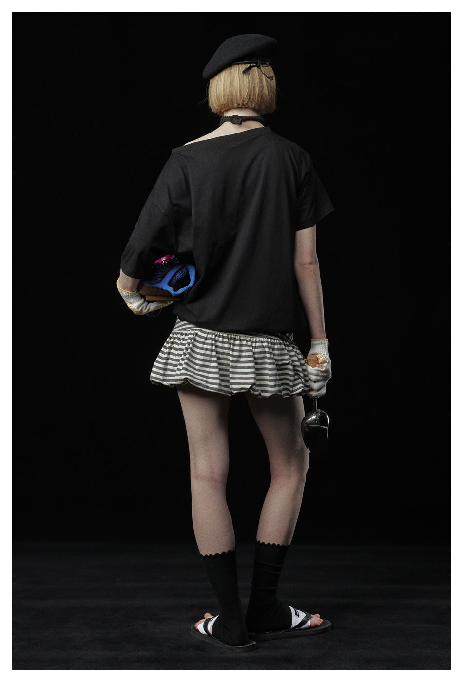 Rear view of a model wearing a plain black oversized T-shirt and a short gray-and-white striped ruffle skirt.