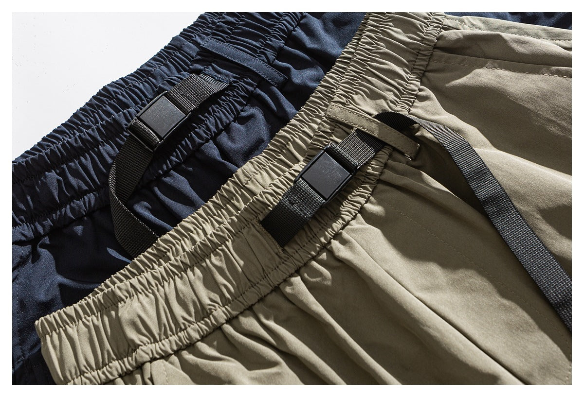 Close-up of navy and khaki trousers with gathered elastic waistbands and black webbing buckle straps.