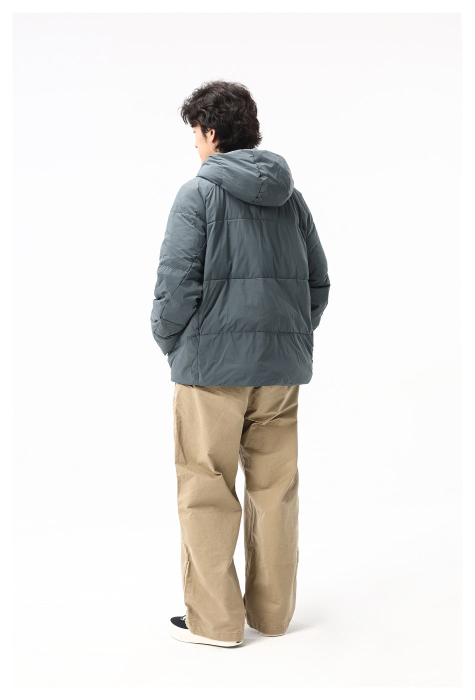 Rear view of a model wearing a slate-gray hooded puffer jacket and tan trousers.