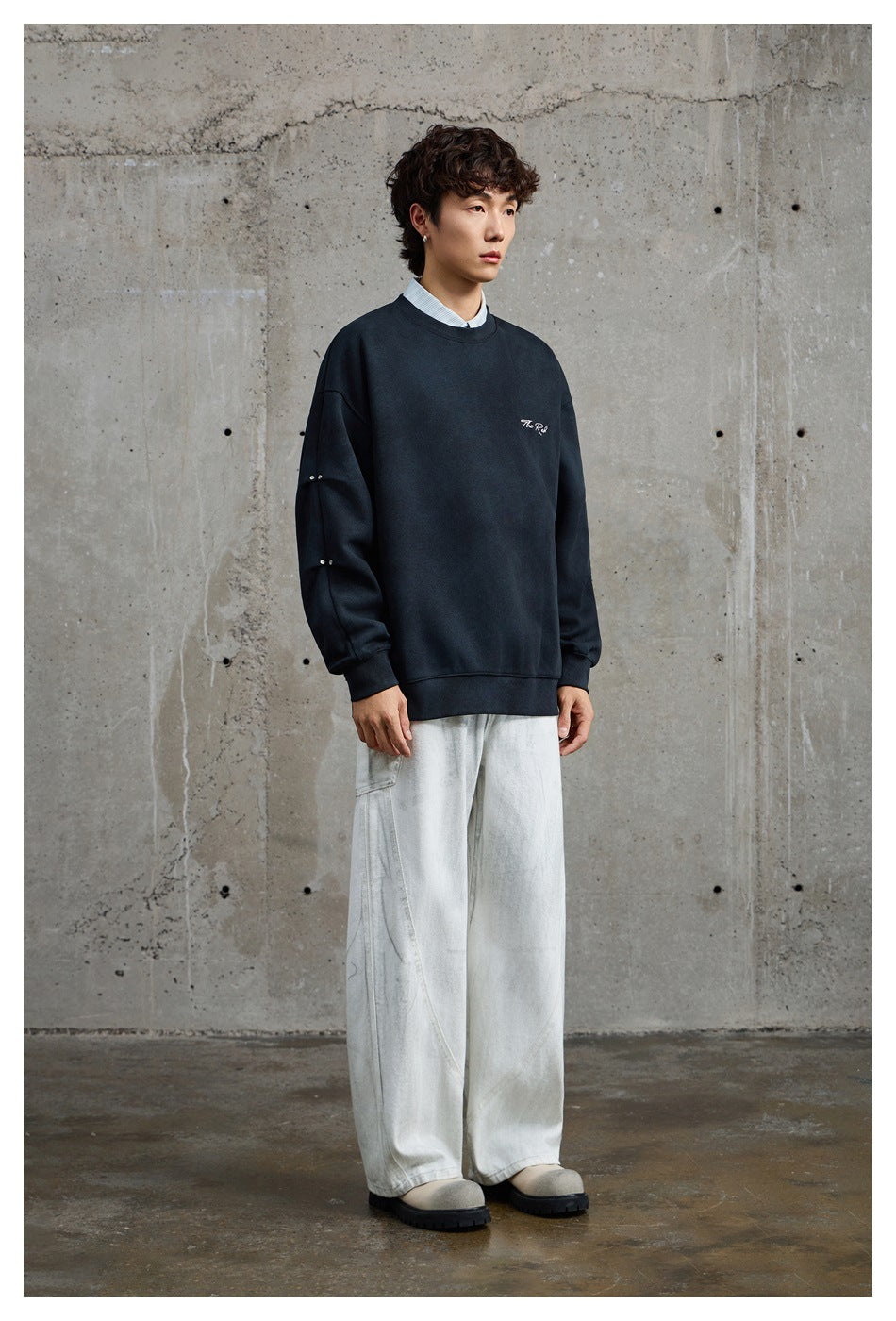 Three-quarter view of a model wearing a dark navy crewneck sweatshirt with white chest script and studded sleeves.