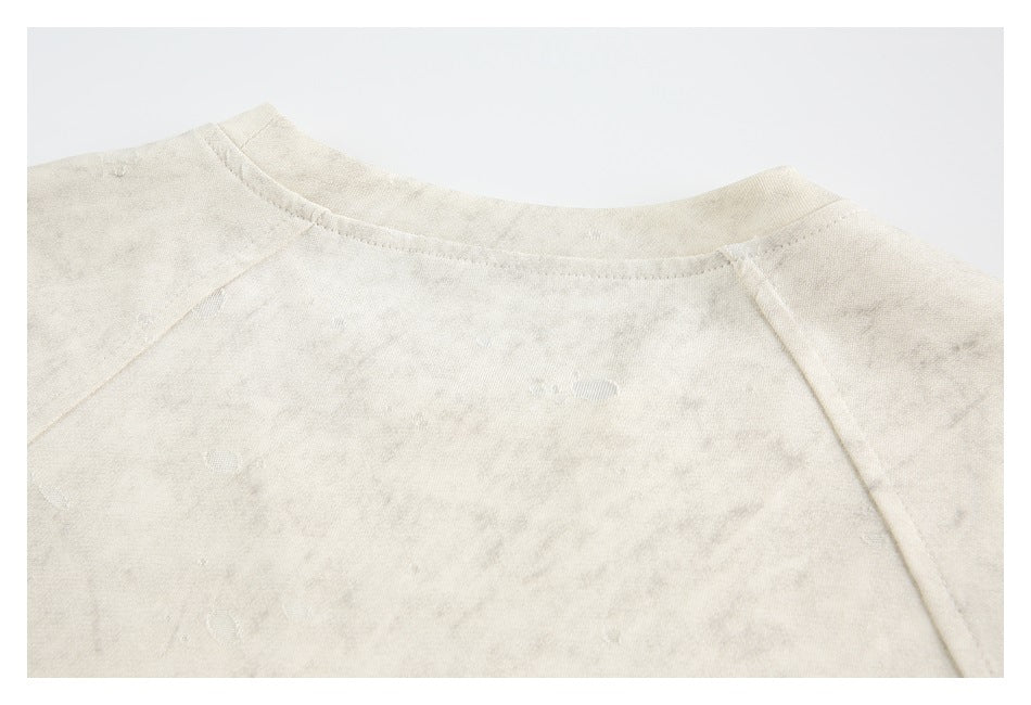 Close-up of an ivory garment neckline with raglan seams and a mottled distressed pattern.