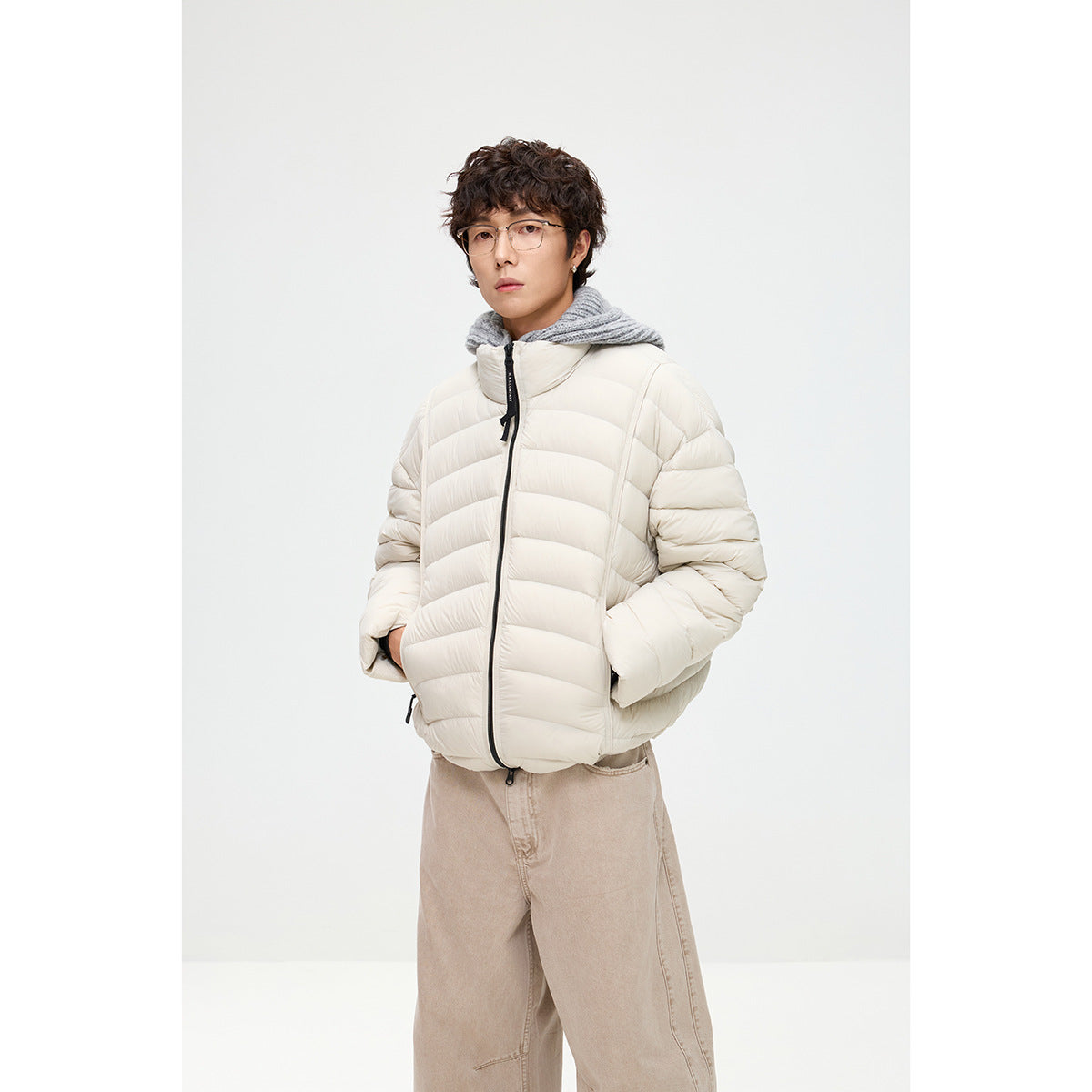 Closer front view of a model in an off-white quilted puffer jacket with black zipper details and a gray hood.