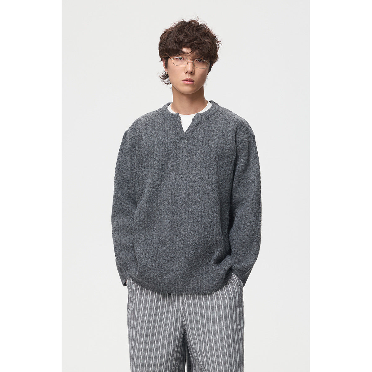 Front view of a model wearing a charcoal gray split-neck sweater over a white shirt with striped trousers.