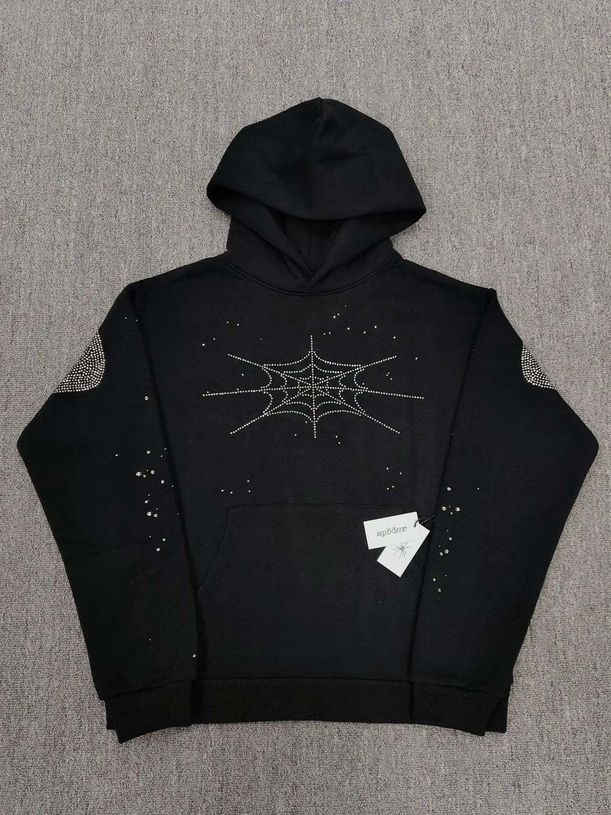 Sp5der black pullover hoodie with silver rhinestone spider web design on chest and shoulders laid flat on grey surface