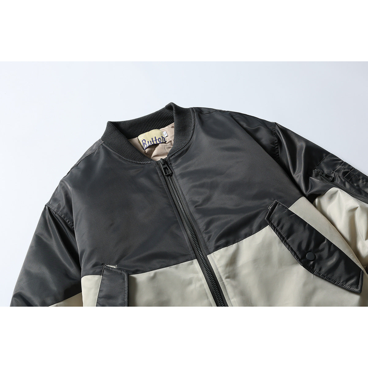Close-up of a black and light gray color-block bomber jacket, showing its ribbed collar, front zipper, and flap pockets.