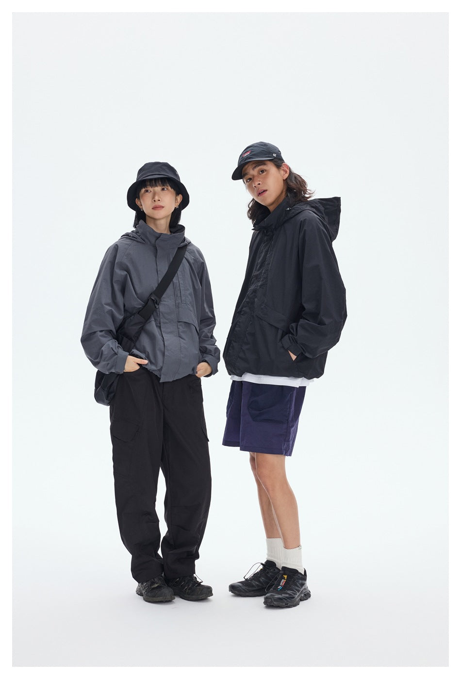Two models wearing hooded jackets: one slate gray with black pants, the other black with purple shorts.