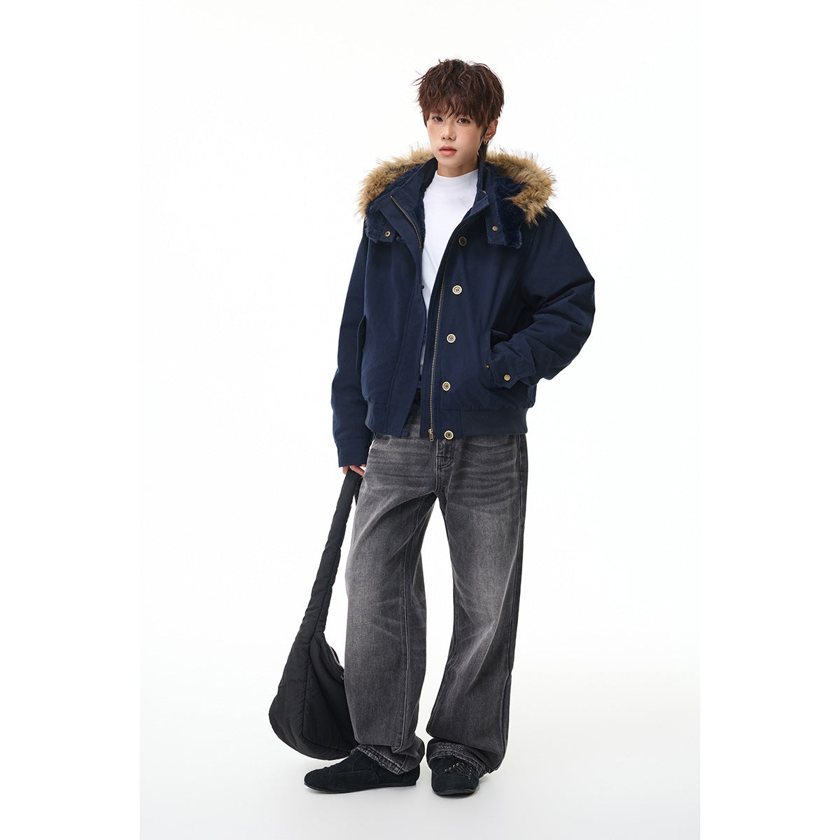 Model wearing a navy hooded jacket with tan fur trim and brass-tone buttons, paired with gray jeans.