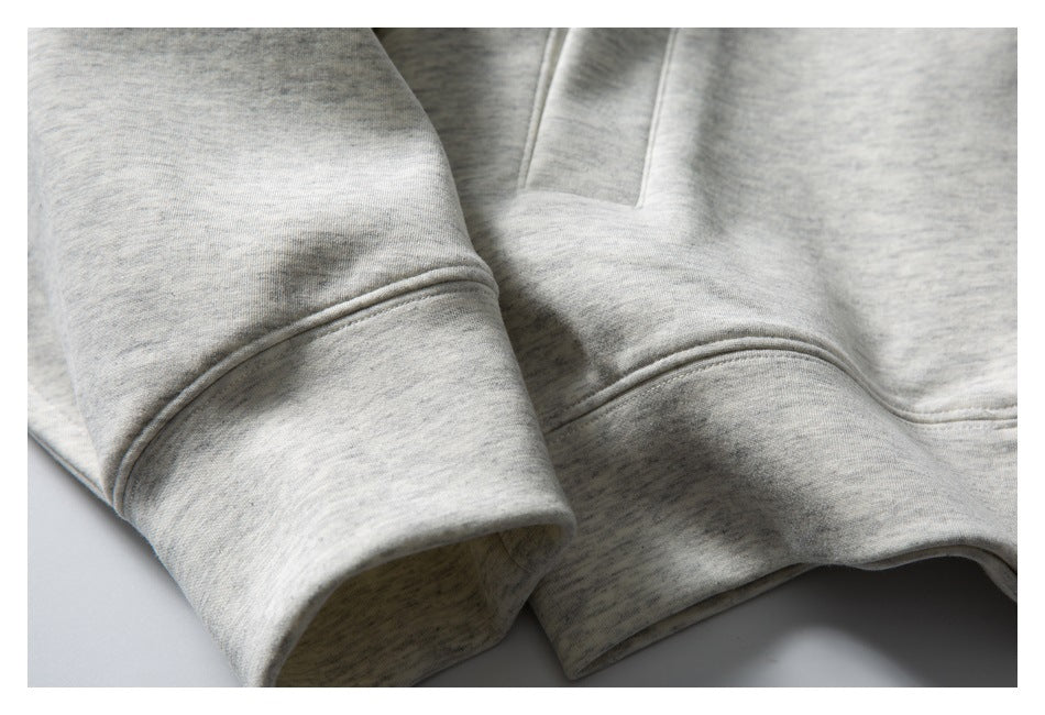 Close-up of a light gray marled sweatshirt showing a sleeve cuff and front pocket seam.