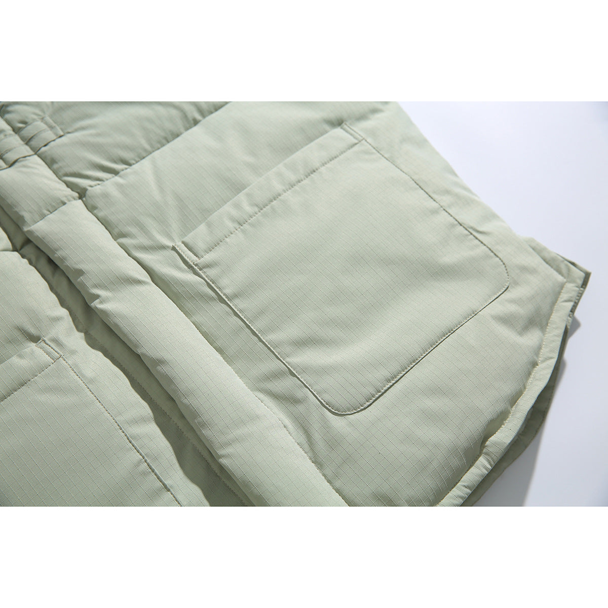 Close-up of a pale sage padded jacket pocket and quilted fabric.