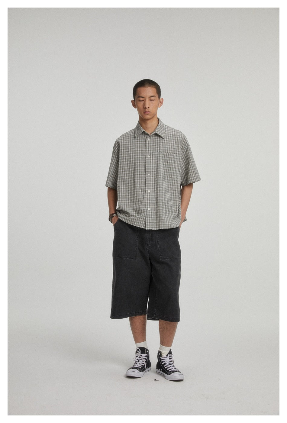 Front view of a model wearing a gray plaid short-sleeve button-up shirt and black knee-length shorts.