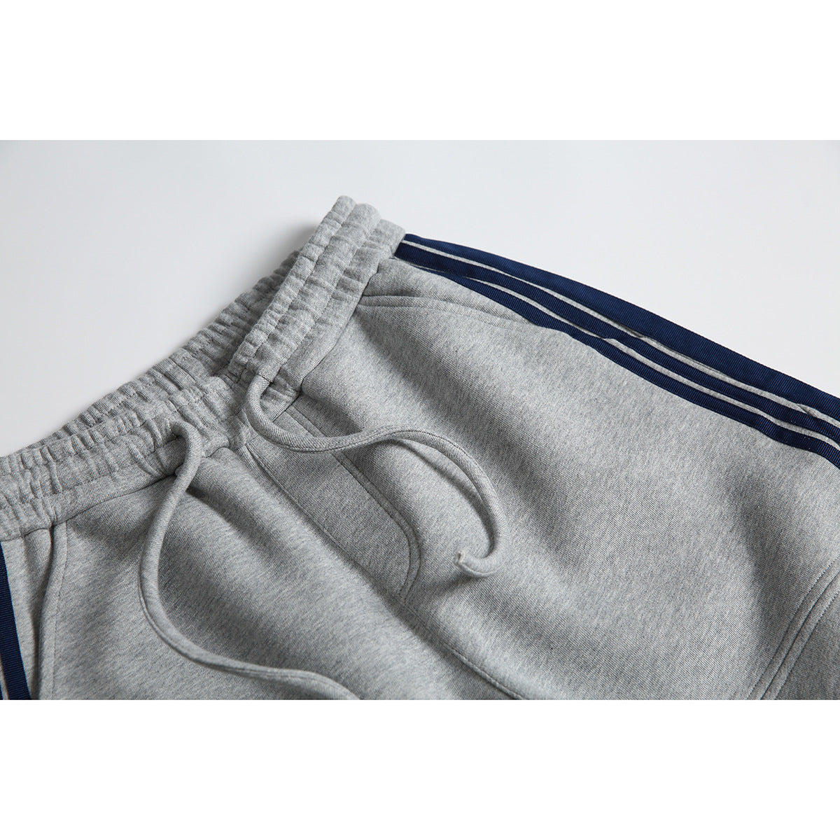 Close-up of gray jogger pants showing the elastic waistband, drawstring, and navy side stripes.