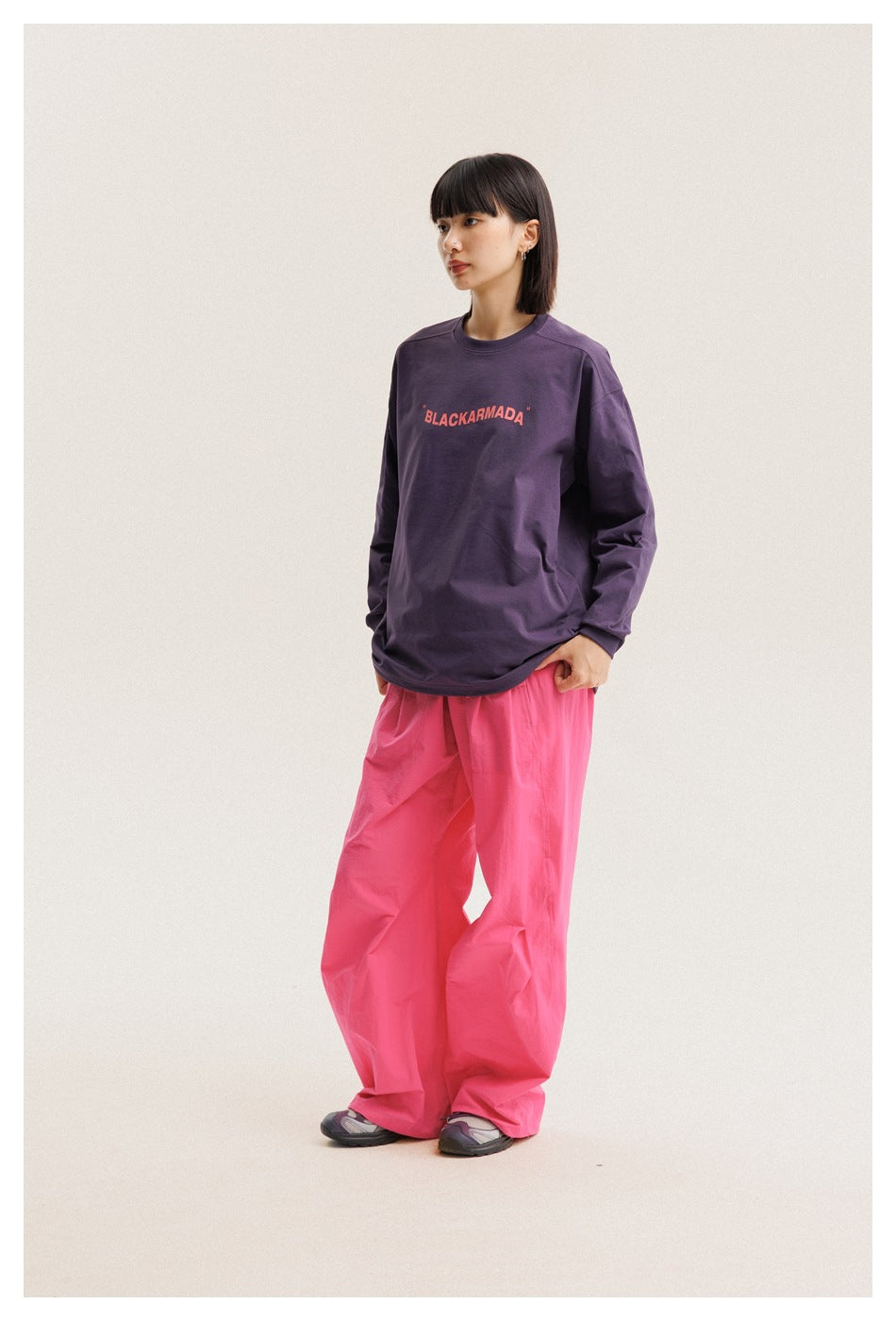 Model wearing a purple long-sleeve shirt with coral chest lettering and bright pink wide-leg pants.