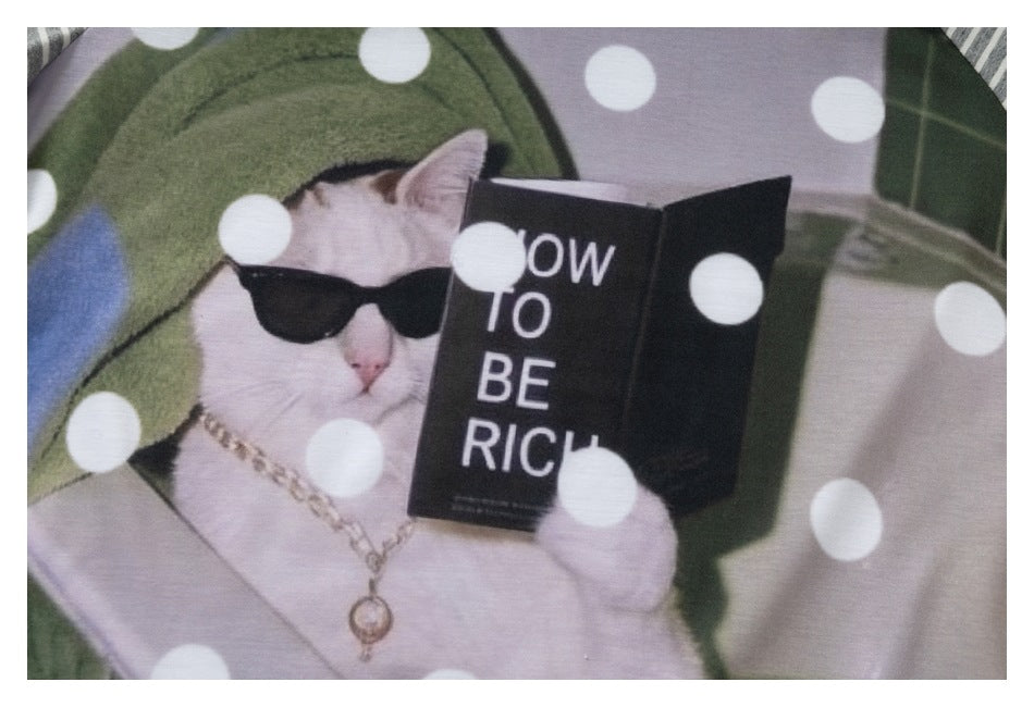 Close-up of the shirt's printed white cat wearing sunglasses and a chain, holding a book among white polka dots.