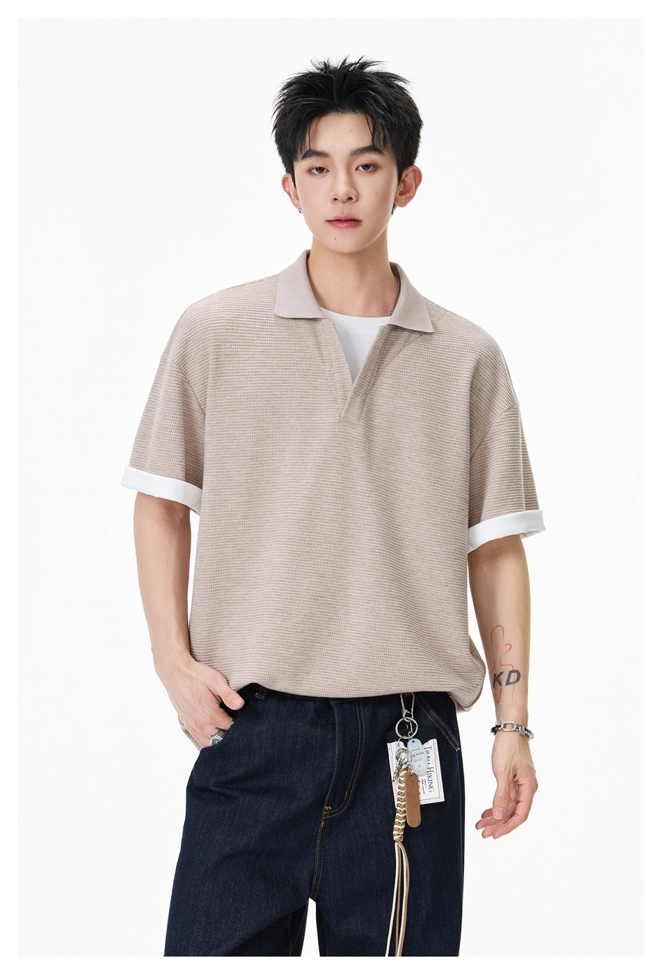 Front view of a model wearing a beige textured polo with a collar, open V-neck, and white turned-up cuffs.