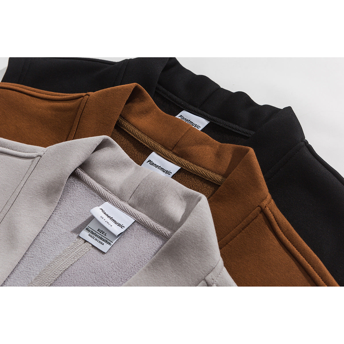 Close-up of the inside collars of taupe, rust-brown, and black sleeveless vests with sewn labels.