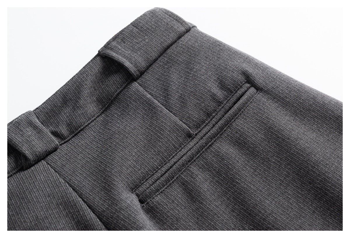 Close-up of charcoal gray trousers showing a belt loop, waistband seam, and rear welt pocket.