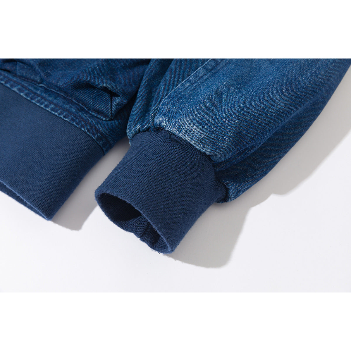 Close-up of two blue denim jacket sleeves with dark ribbed cuffs.