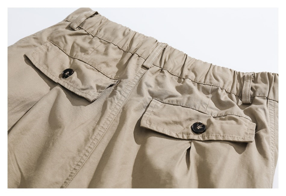 Close-up of khaki trousers with an elastic waistband, belt loops, and buttoned flap pockets.