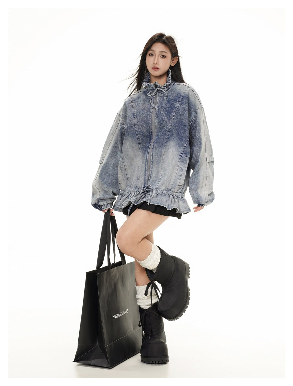 Model wearing an oversized blue washed denim jacket with ruffled drawstring hem, holding a black bag, with black boots