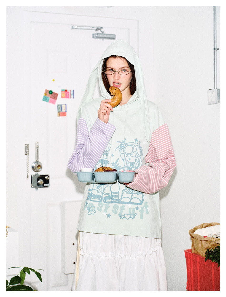 Closer view of a model wearing a pale mint graphic hoodie with long hood panels and pink and lilac striped sleeves.