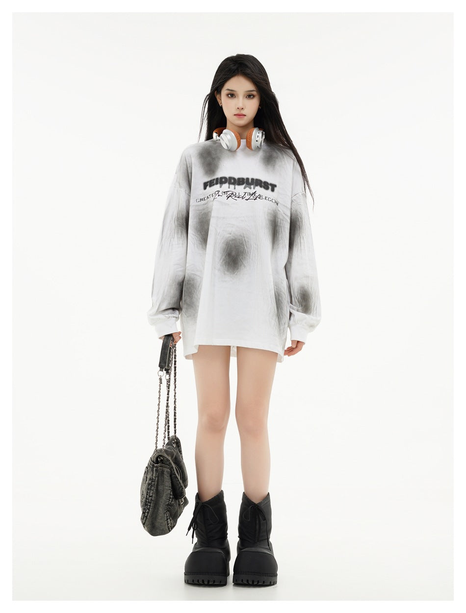 Full-length model wearing an oversized white and gray tie-dye shirt with black chest lettering and carrying a dark bag.
