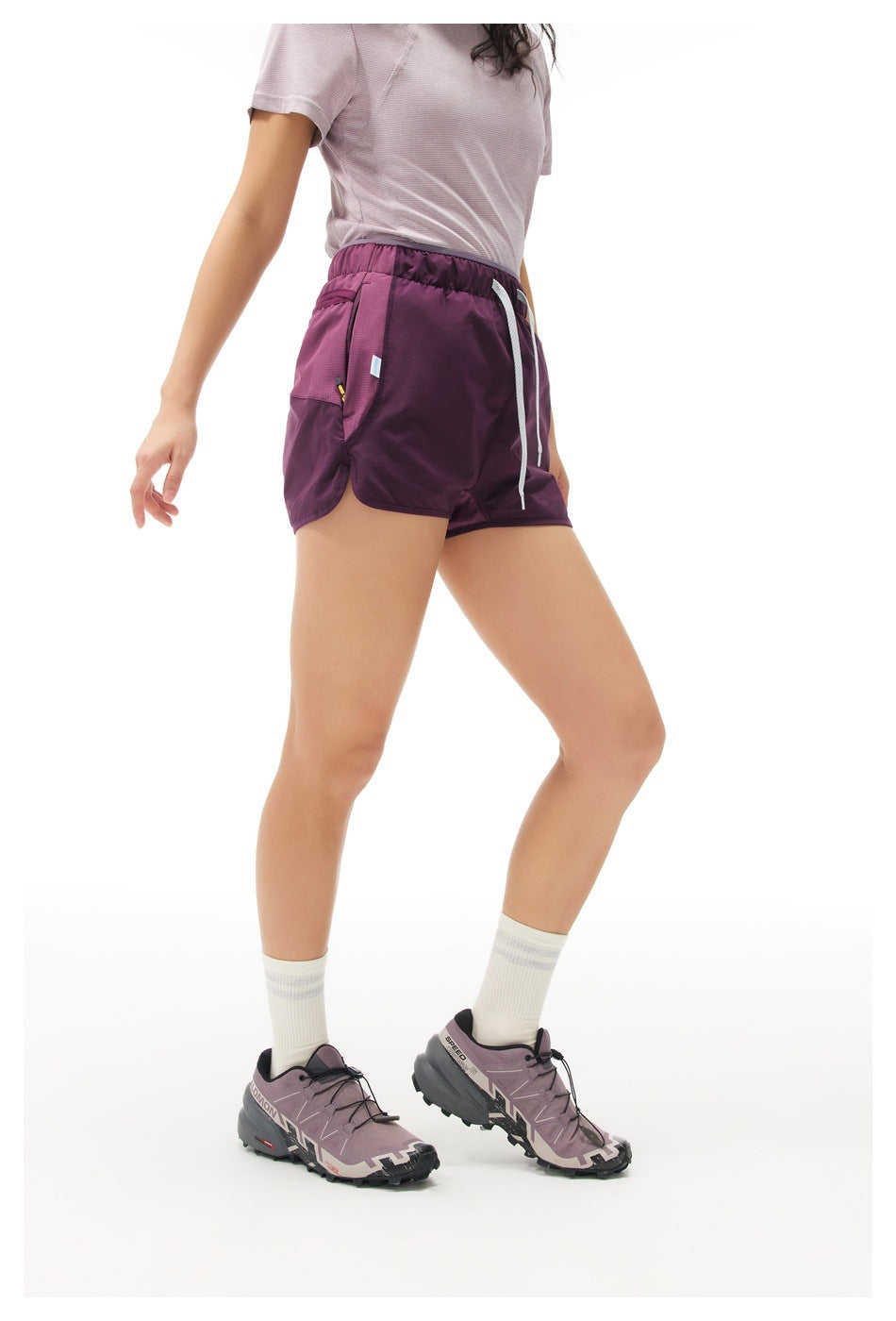 Angled side view of a model wearing plum running shorts with a white drawstring and side pocket.