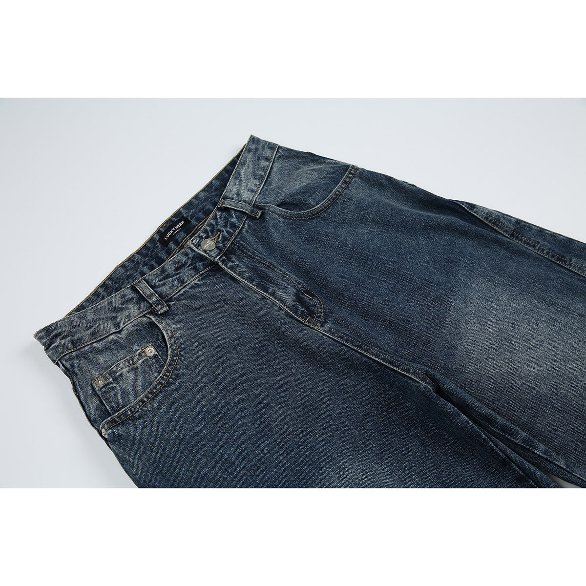 Close-up of dark blue washed jeans showing the front waistband, button, belt loops, and front pocket.