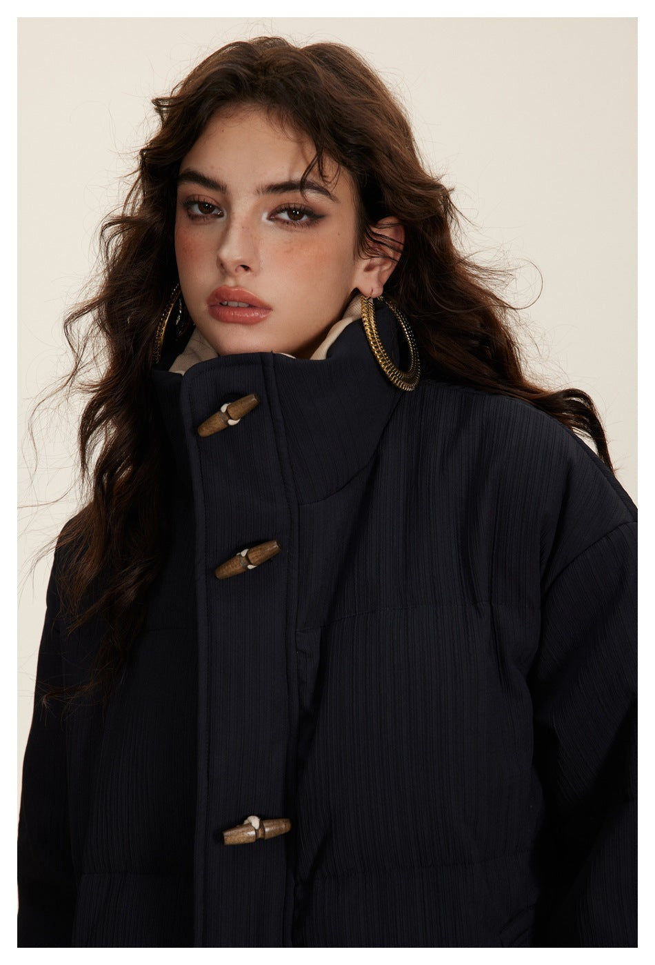 Close-up of a model wearing a dark navy padded jacket with a high collar and wooden toggle fasteners.
