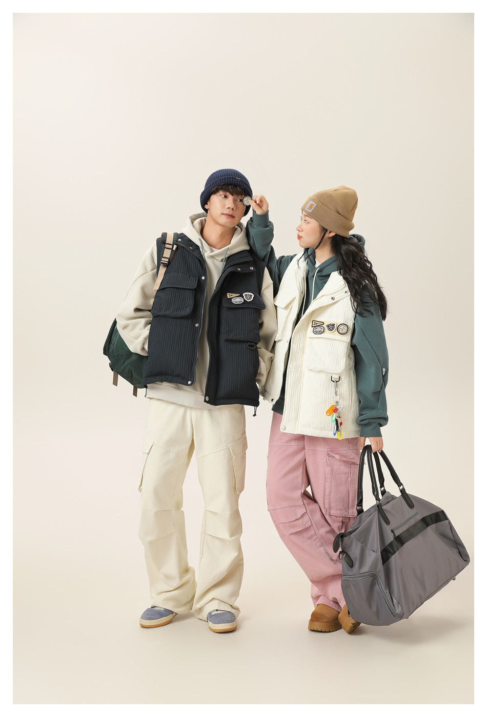 Full-length view of two models wearing navy and cream utility vests over hoodies with cargo pants.