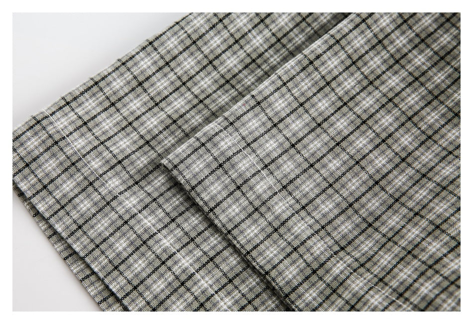 Gray and beige plaid fabric with black grid lines arranged in overlapping folds.