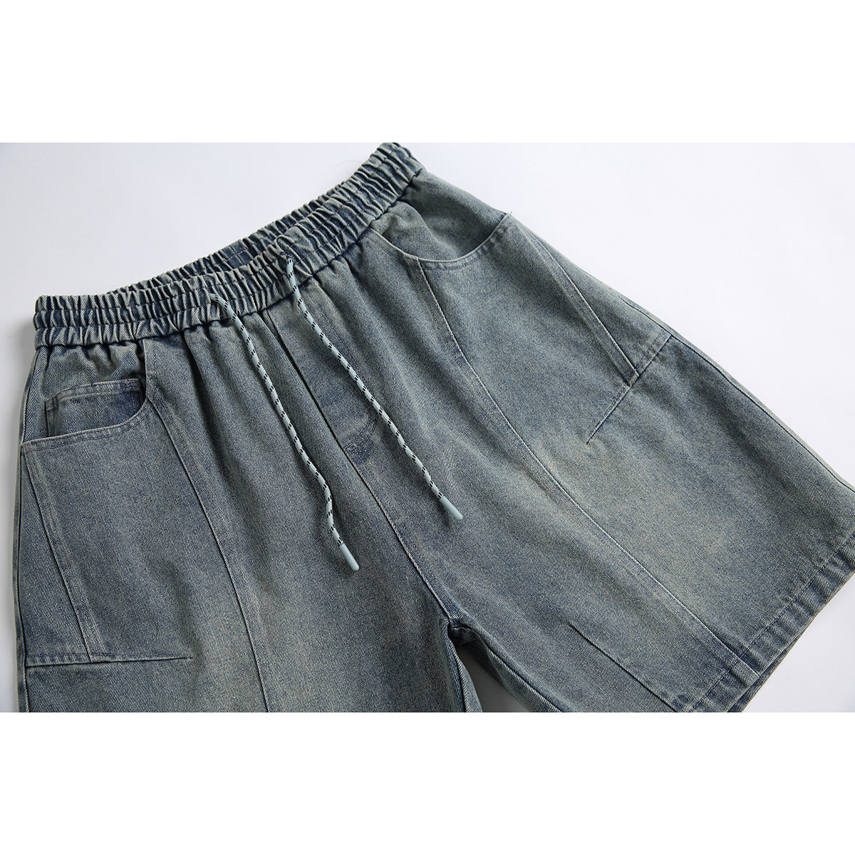 Close view of gray-blue denim shorts with an elastic drawstring waist, large pockets and panel seams.