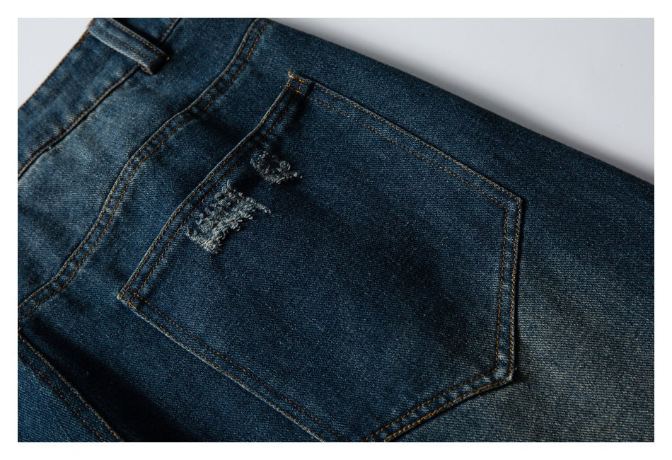 Close-up of a rear pocket on dark blue jeans with small distressed patches and contrast stitching.
