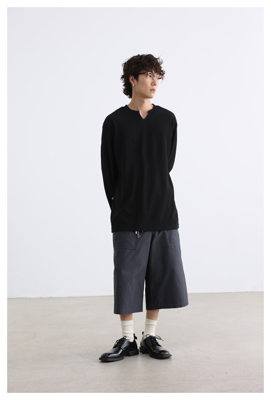 Model wearing a black long-sleeve shirt with a notched neckline and charcoal wide-leg shorts.