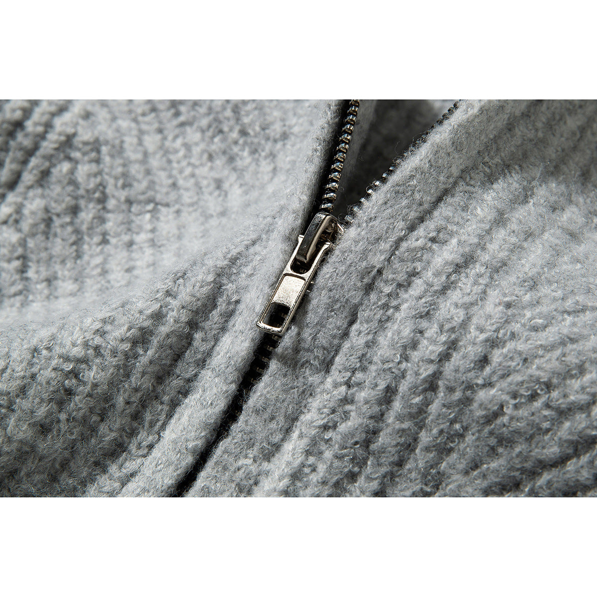 Close-up of a metal zipper pull against the textured light gray knit sweater.