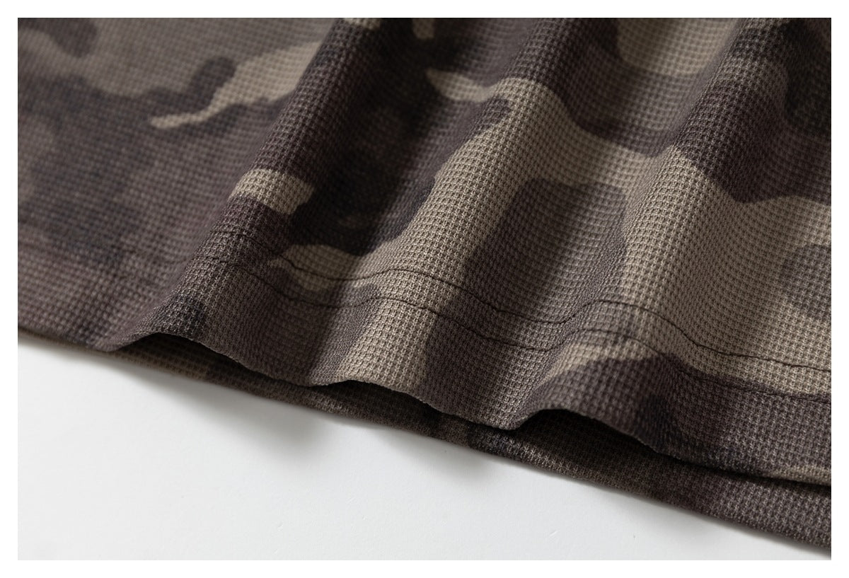 Close-up of the stitched bottom hem on gray-brown camouflage fabric.