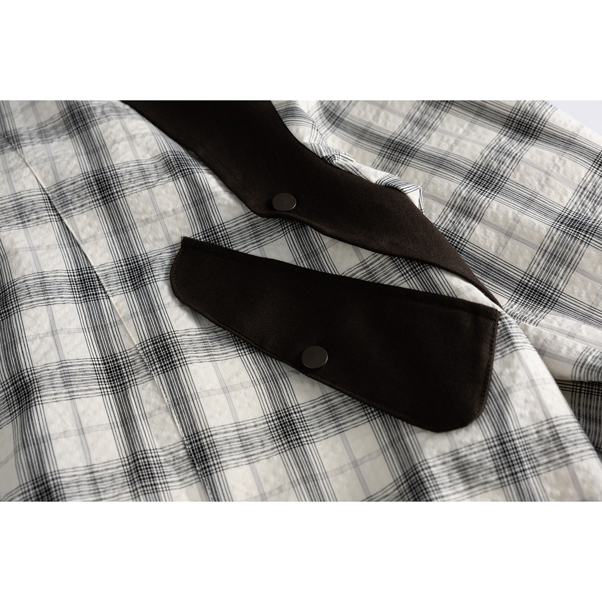 Close-up of the black-and-white plaid jacket front with dark brown snap-button trim.
